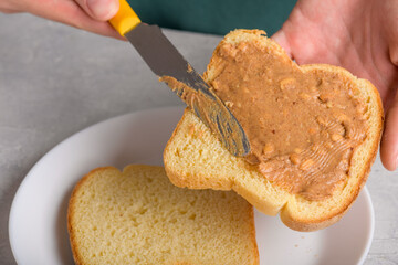 Close up of white bread toast with spreading peanut butter and knife, woman's hands spread peanut butter, close up, Typical snack food, lifestyle, domestic life, preparing american breakfast