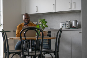 Man using laptop and smart phone at table in kitchen