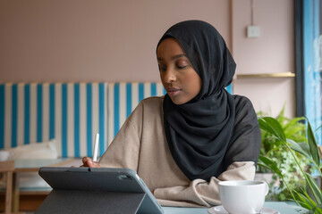 Young woman in hijab working on tablet in cafe