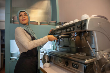 Young woman in hijab making coffee in cafe - obrazy, fototapety, plakaty