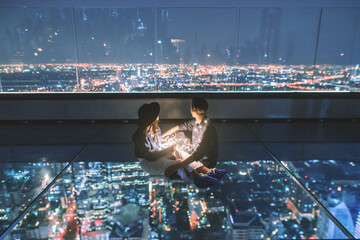 Couple sitting and looking at the city view - obrazy, fototapety, plakaty