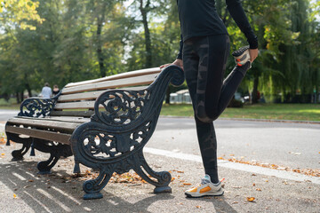 Low section of woman stretching leg at bench in park - Powered by Adobe