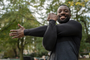 Portrait of smiling athletic man stretching arm in park