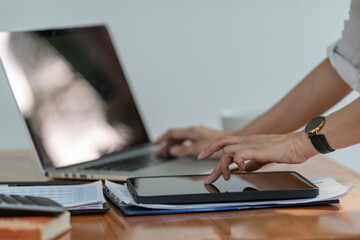 Businesswoman using a digital tablet and laptop computer at the office. A businesswoman working, touching a tablet screen and typing on a laptop computer, searching business data, surfing the internet