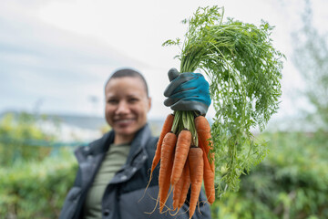 Portrait of smiling woman holding bunch of carrots in urban garden