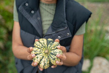 Mid section of woman holding homegrown gourd in urban garden - obrazy, fototapety, plakaty