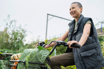 Smiling woman riding cargo electric trike loaded with homegrown vegetables