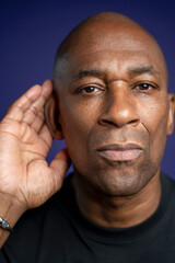 Portrait of serious man with hand on ear against purple background
