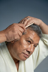 Portrait of serious man combing hair against gray background