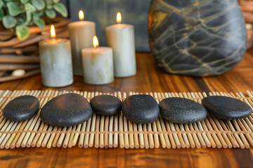 Fototapeta na wymiar Hot stones arranged on a bamboo mat, ready for a massage, with essential oils and candles in the background, setting a tranquil mood
