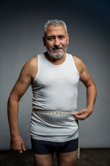 Portrait of man measuring waist against gray background