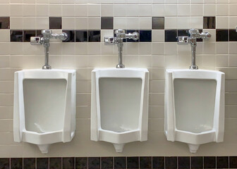 Three urinals in a row on a while with checkered wall tile