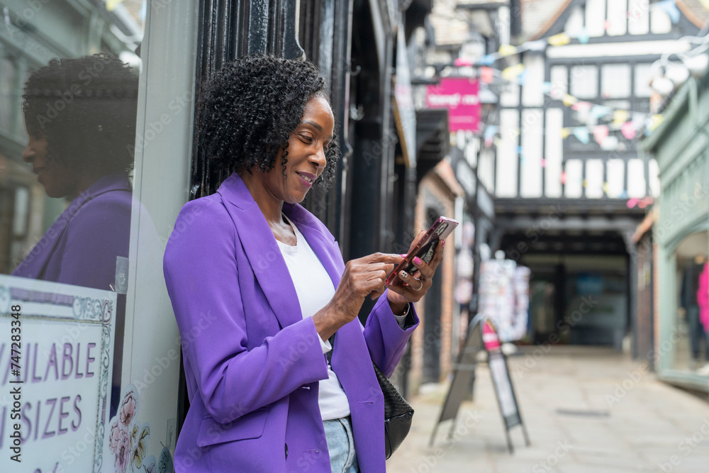 Fototapete smiling woman using smart phone while standing by building