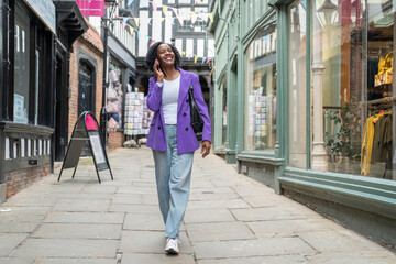 Smiling woman talking by smart phone while walking in city