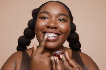 Studio shot of smiling young woman applying lip moisturizer