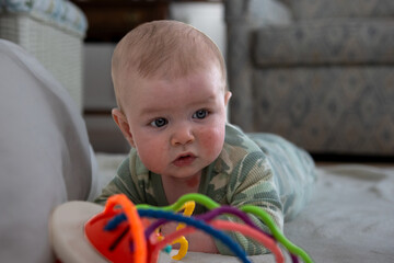 Four month old baby boy on the floor with a toy.