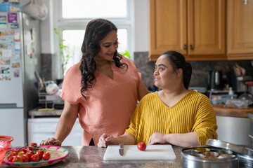 Portrait of mother with down syndrome daughter preparing food in kitchen