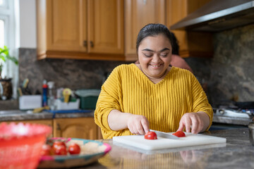 Smiling woman with down syndrome cutting tomato in kitchen