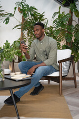 Young man with smartphone sitting in office lounge