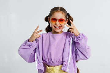 Preteen kid girl in summer style and sunglasses showing rock and roll sign on white background