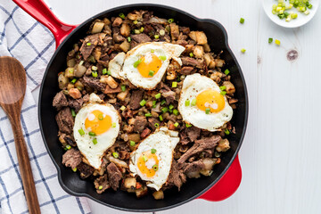 A frying pan of roast beef hash topped with fried eggs, ready for serving.