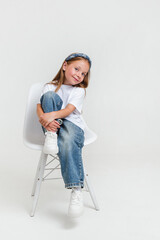 Stylish kid girl wearing white t-shirt and jeans looking at camera sitting in studio
