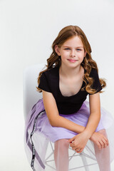 Smiling preteen girl in black t-shirt, violet skirt and white sneakers posing and sitting on white background