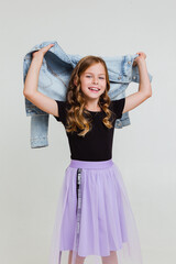 Smiling preteen girl in black t-shirt, violet skirt and white sneakers posing and standing on white background
