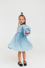 Happy cute little girl in blue dress smiling and dancing on white background. Soft motion focus