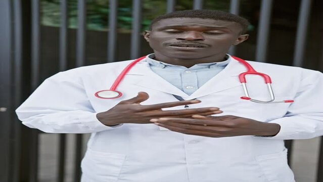Confident african male doctor with stethoscope posing outdoors in urban setting.