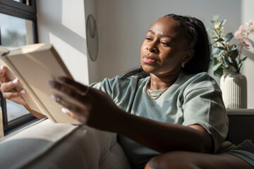 Young woman reading book while resting at home