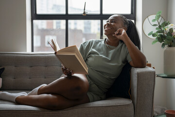 Young woman reading book while resting on sofa at home