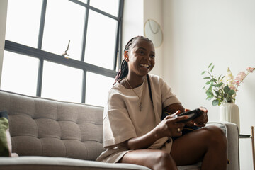 Excited young woman playing video games while sitting on sofa at home