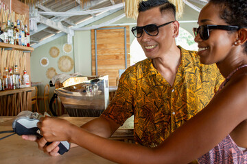 Smiling friends paying with card in beach bar