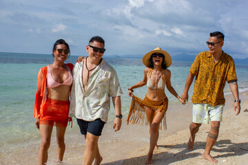 Smiling friends holding hands and walking on beach