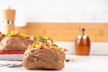 Homemade baked potato with various toppings - meat, sausages, vegetables, cheese, with white cheesy...