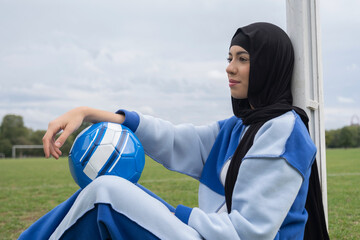Portrait of woman in hijab sitting in soccer field with soccer ball