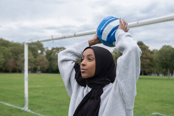 Smiling woman in hijab throwing soccer ball in park - obrazy, fototapety, plakaty