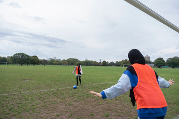 Two women in hijabs playing soccer in park