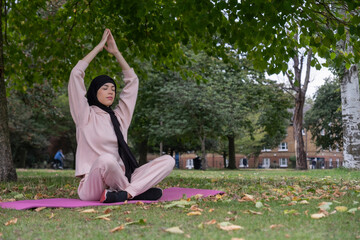 Woman in hijab and pink tracksuit meditating in park