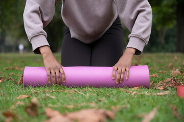 Low section of woman rolling up yoga mat on grass in park