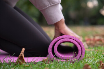 Close-up of woman rolling up yoga mat on grass in park - obrazy, fototapety, plakaty