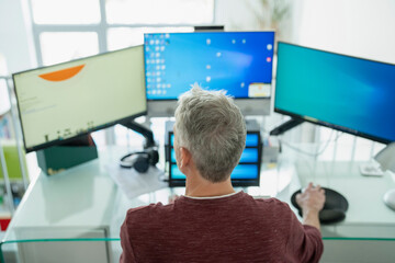 Mature man working on three monitors at home
