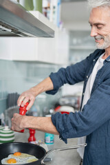 Smiling mature man seasoning eggs in pan