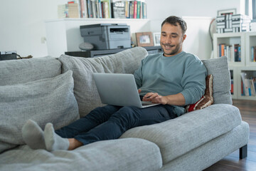 Obraz premium Smiling mature man working on laptop on sofa