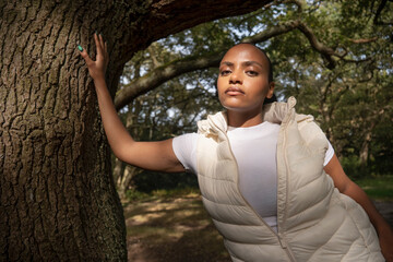 Portrait of young woman leaning on tree trunk in park on sunny day