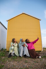 Three Muslim friends taking selfie while sitting by beach hut