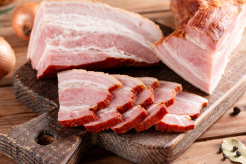 Whole Smoked Slab Bacon. Brisket. Sliced smoked gammon on a wooden table with pepper, salt, and garlic on cutting board on a wooden table