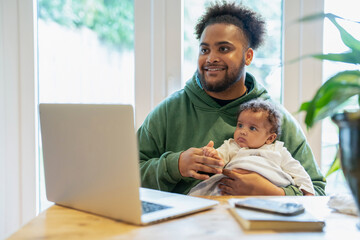 Father holding baby daughter in front of laptop at home