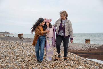 Grandmother, mother and daughter walking on beach on cloudy day